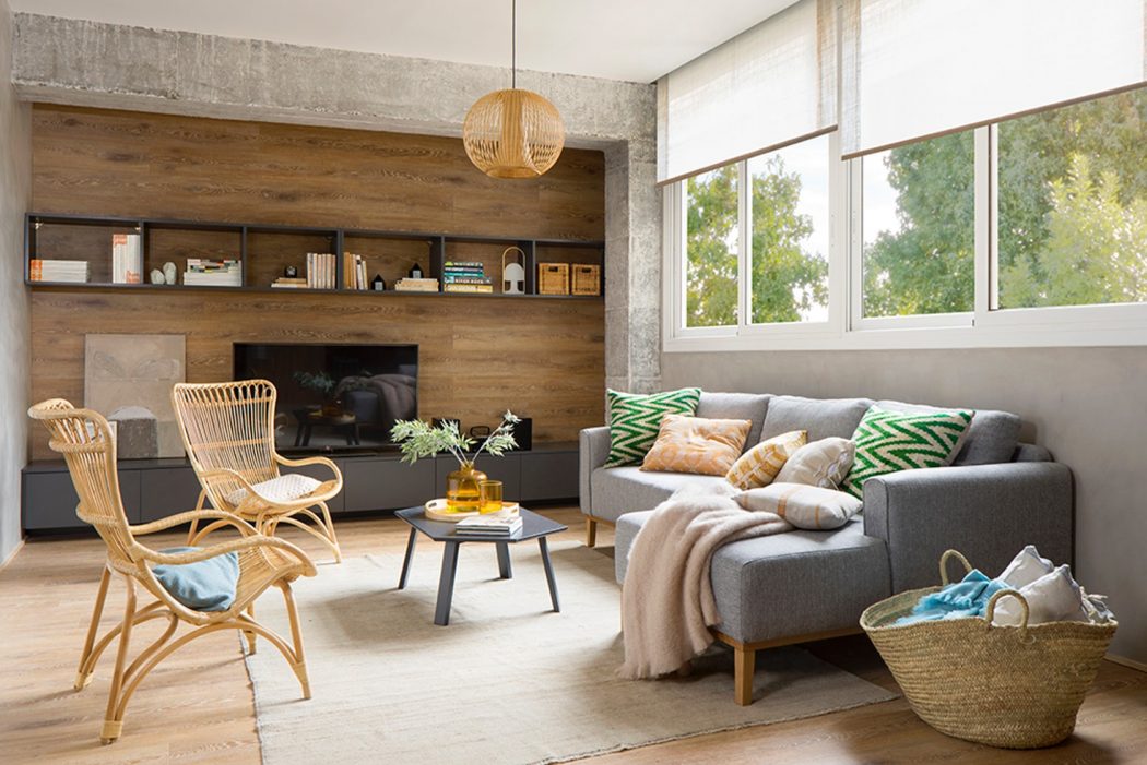 Cozy living room with wooden accent wall, plush gray sofa, and rustic rattan chairs.