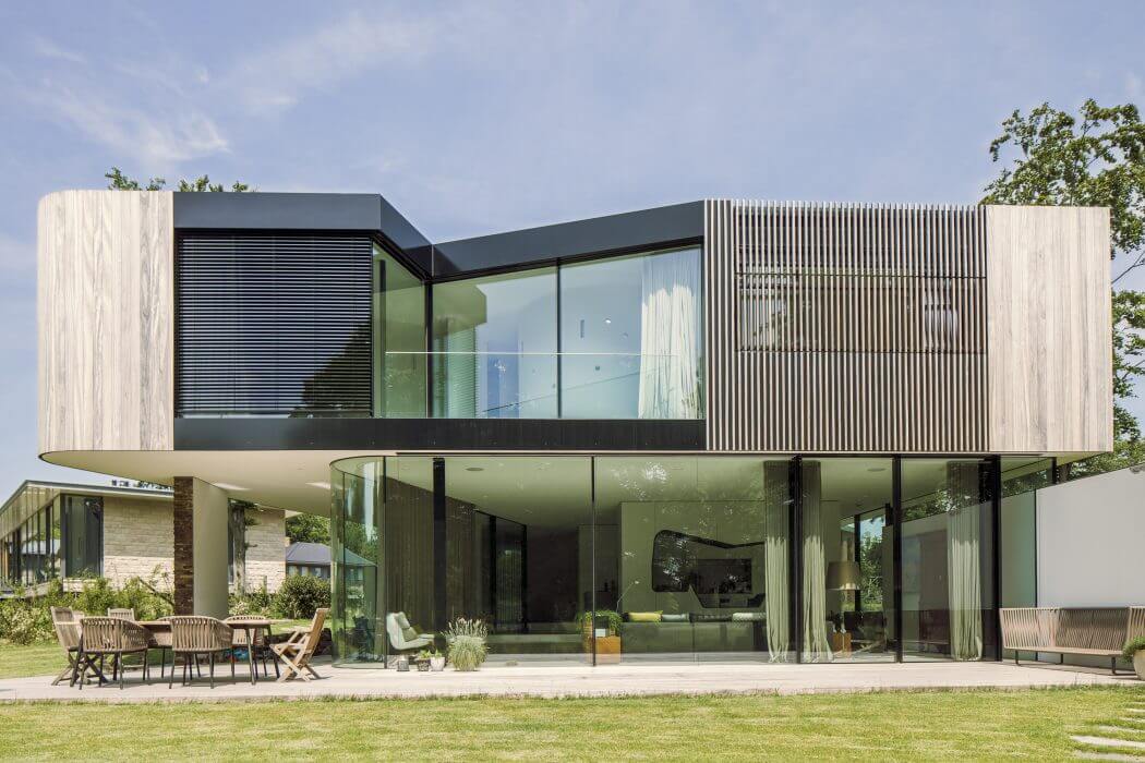 A modern, glass-walled home with a cantilevered upper level, surrounded by lush greenery.