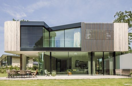 A modern, glass-walled home with a cantilevered upper level, surrounded by lush greenery.