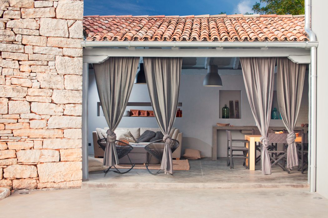 Cozy outdoor living space with stone walls, tiled roof, and curtained entryway.