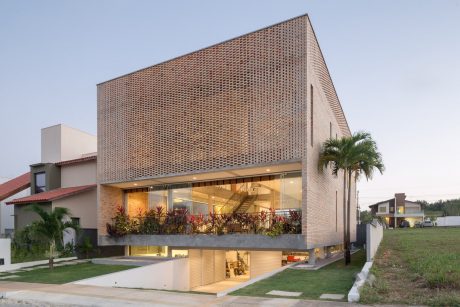A modern, brick-clad building with large glass walls and a prominent balcony featuring tropical plants.