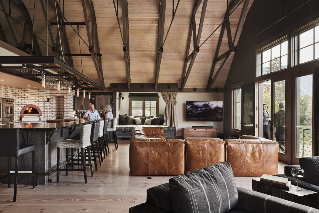 Rustic open-concept living room with wooden beams, brick fireplace, and leather sofas.