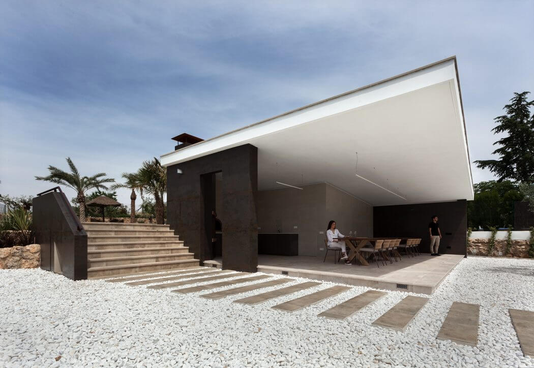A modern, minimalist structure with clean lines, an expansive covered patio, and steps leading to the entrance.