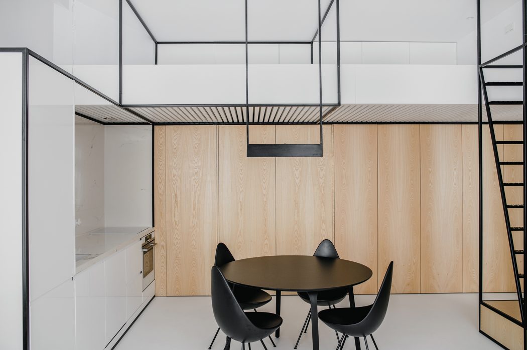 Minimalist interior with wooden panels, metal frame, round table, and black chairs.