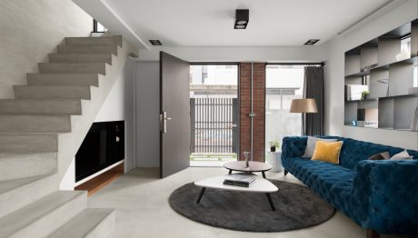 Minimalist living room with concrete stairs, blue couch, round area rug, and built-in storage.