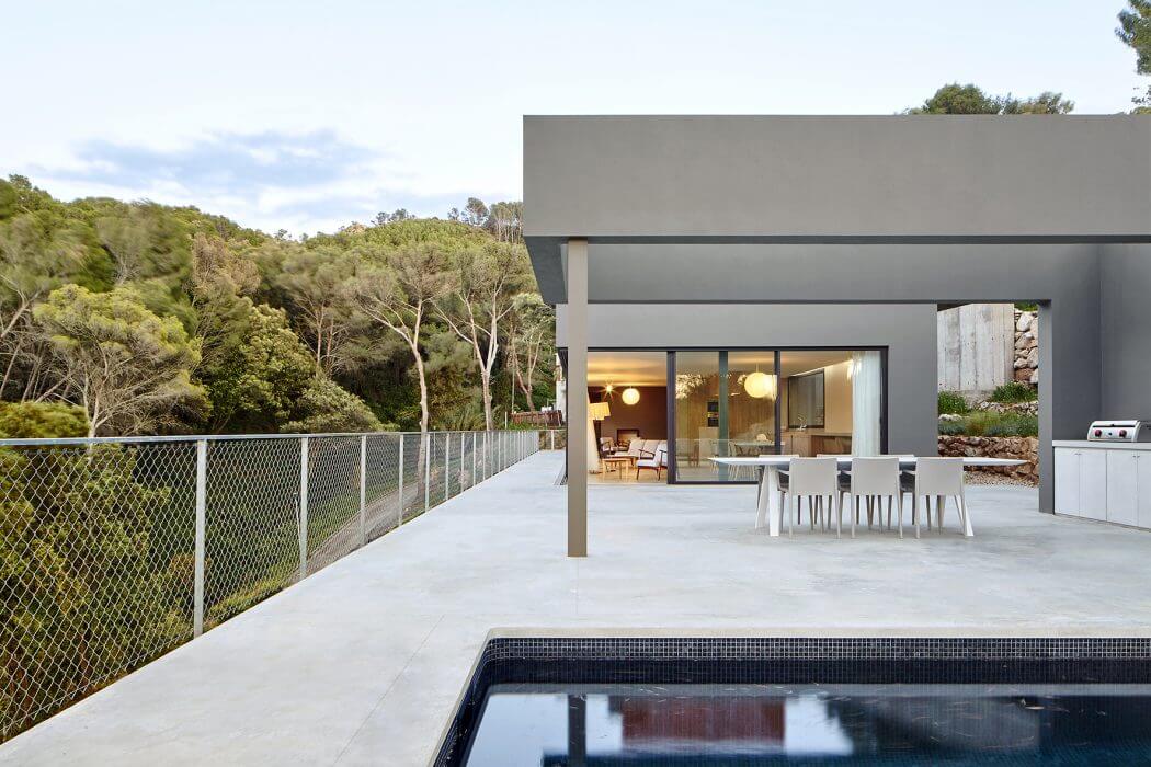 Modern outdoor terrace with sleek concrete and metal design, pool, and distant wooded view.