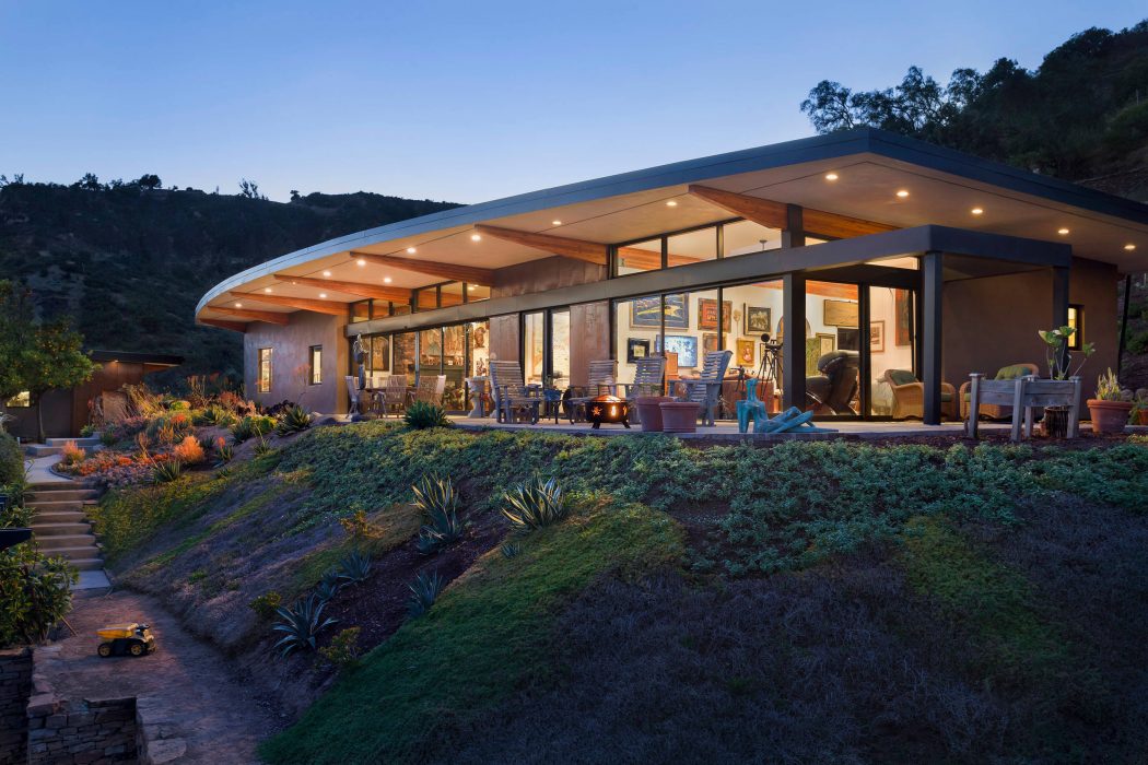 Modern, open-concept home with wood and glass features, surrounded by lush landscaping.