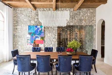 Rustic dining room with stone walls, wooden beams, and modern blue velvet chairs.