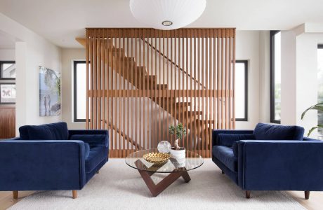 A modern living room with a wooden slat partition, glass coffee table, and navy blue sofas.