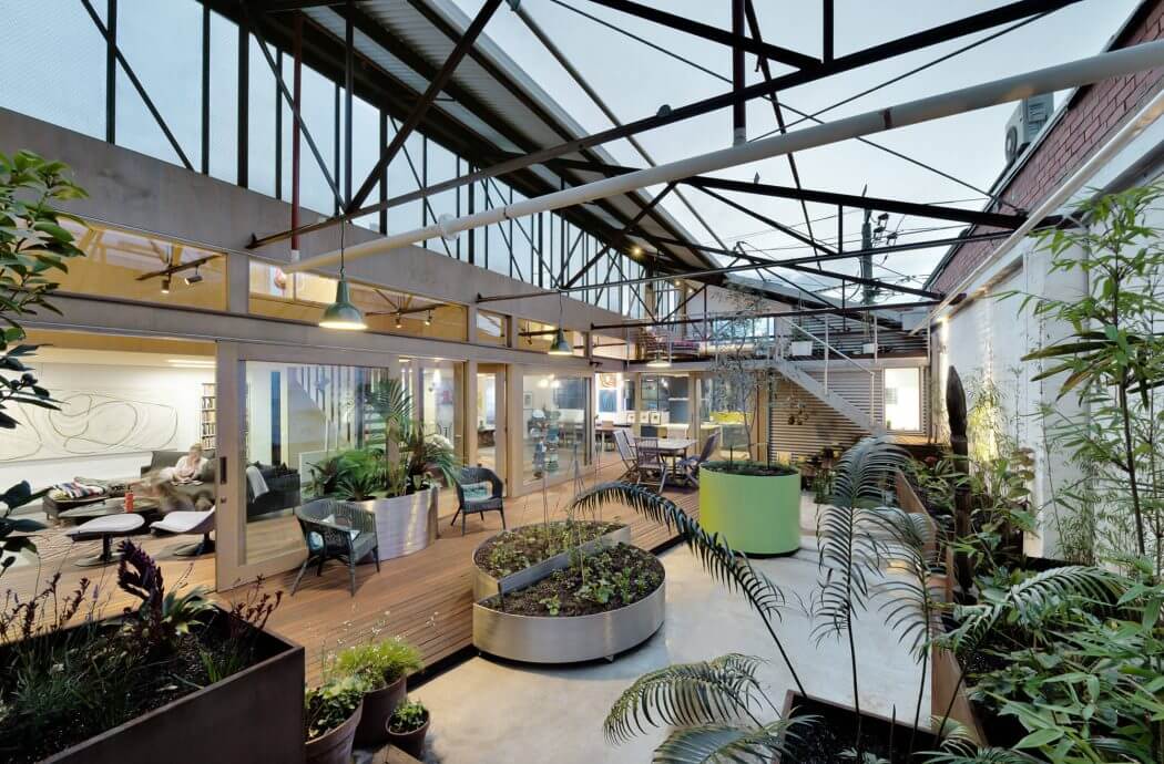 A spacious indoor greenhouse with glass walls, steel beams, and lush greenery.