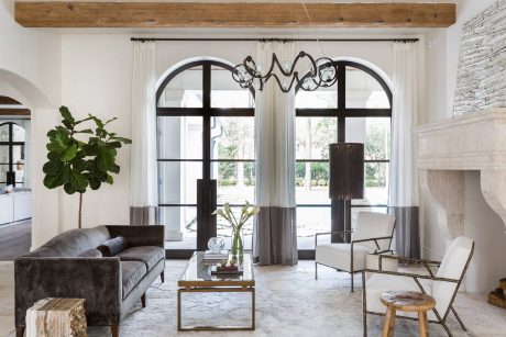 Rustic living space with arched windows, wood beams, and metal chandeliers.