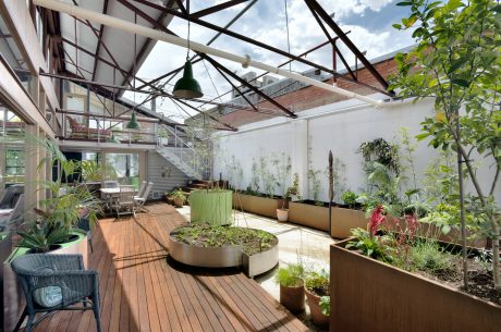 A modern indoor-outdoor greenhouse-like space with a lush, manicured garden and wooden deck.