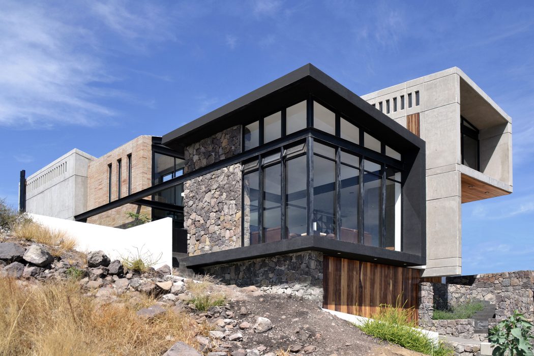 Modern mountain home with stone, glass, and wood accents, set on a rocky hillside.