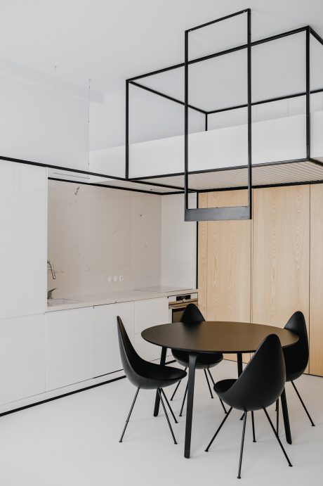 A minimalist kitchen and dining space with sleek black frames, wooden cabinetry, and a round dining table with black chairs.