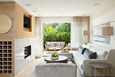 Elegant living room with floor-to-ceiling windows offering scenic outdoor views, warm wood accents.