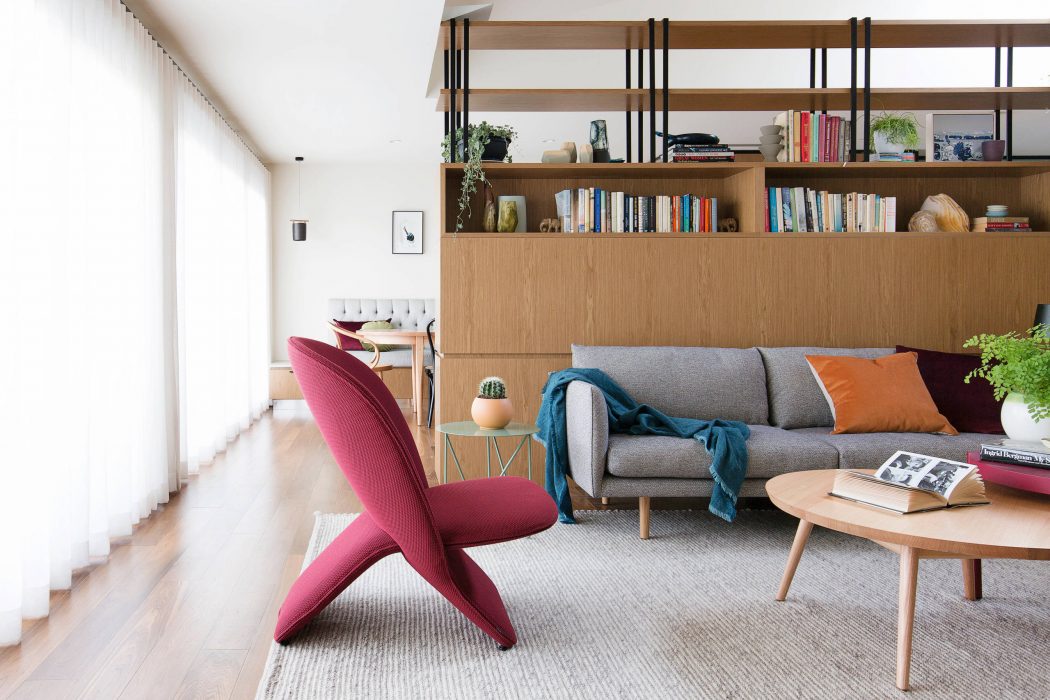 Modern living room with wooden shelving, plush sofa, and vibrant red armchair.