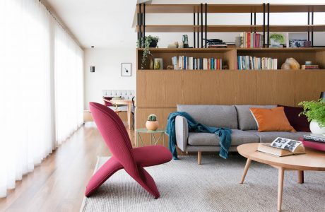 Modern living room with wooden shelving, plush sofa, and vibrant red armchair.