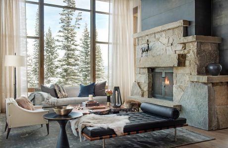 Cozy, rustic living room with stone fireplace, large windows overlooking snowy trees.