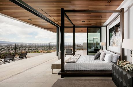 Expansive glass-walled bedroom with wooden ceiling and panoramic city views.