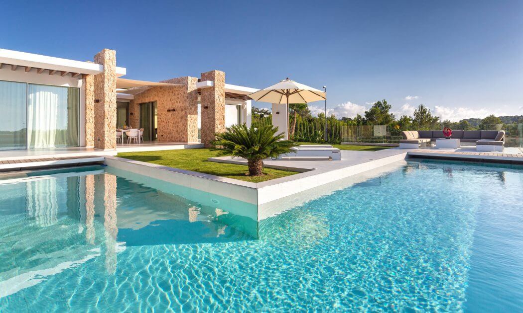 Luxurious modern villa with sleek pool, lush landscaping, and warm stone accents.