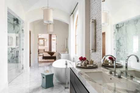 Luxurious marble bathroom with freestanding tub, vanity, and arched doorway to bedroom.