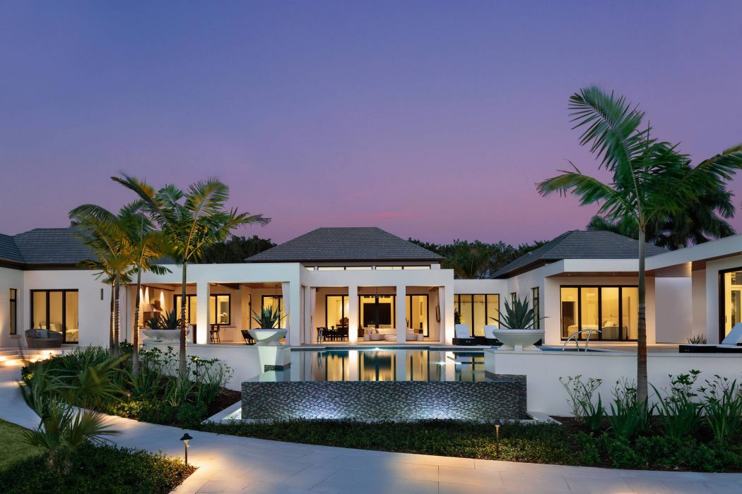 A luxurious villa with palm trees, a reflective pool, and a modern architectural design.