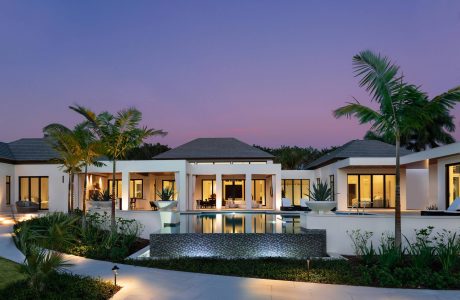 A luxurious villa with palm trees, a reflective pool, and a modern architectural design.