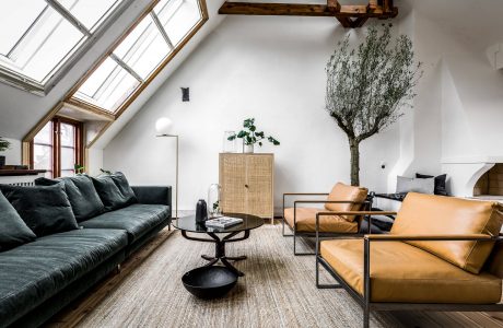 Airy loft-style living room with large windows, wooden beams, and a mix of modern and rustic furnishings.