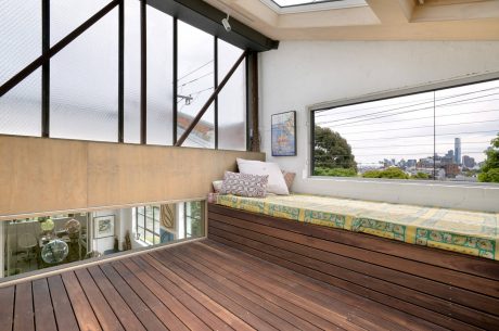 Warm modern interior with wooden deck, glass walls, and an urban city view.