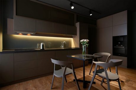 The image depicts a modern, minimalist kitchen with dark cabinets, a sleek countertop, and subtle lighting.