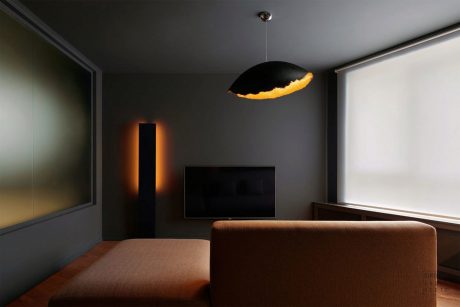 Dark, minimalist living room with black walls, large TV, and unique pendant light casting warm glow.