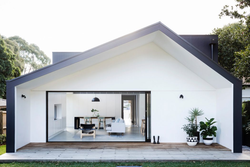 Sleek, modern white home with a gabled roof, large windows, and a deck leading to the interior.