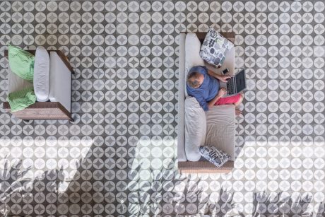 Geometric pattern tile floor, wicker furniture, and person relaxing with laptop.