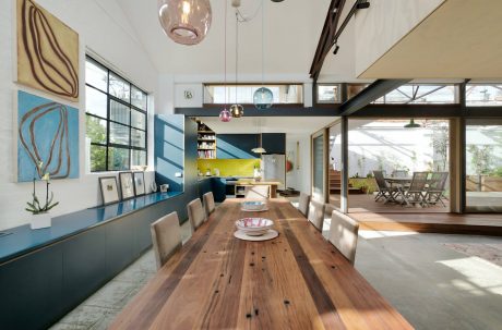An open-concept living area featuring a large wooden dining table, modern pendant lights, and colorful artwork on the walls.