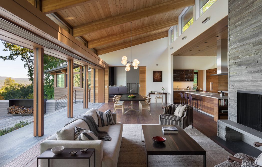 Contemporary living room with high ceilings, wooden beams, and floor-to-ceiling windows overlooking nature.