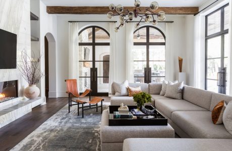 A cozy living room with arched windows, a rustic beam ceiling, and a contemporary chandelier.