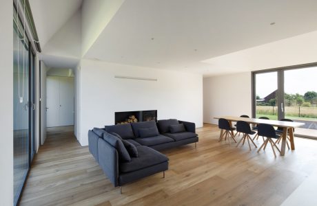 Spacious open-plan living area with large windows, dark furniture, and wooden floors.