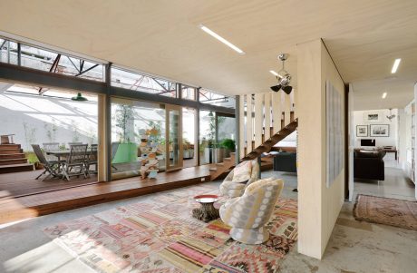 Spacious open-plan living area with large windows, wooden floors, and diverse furnishings.