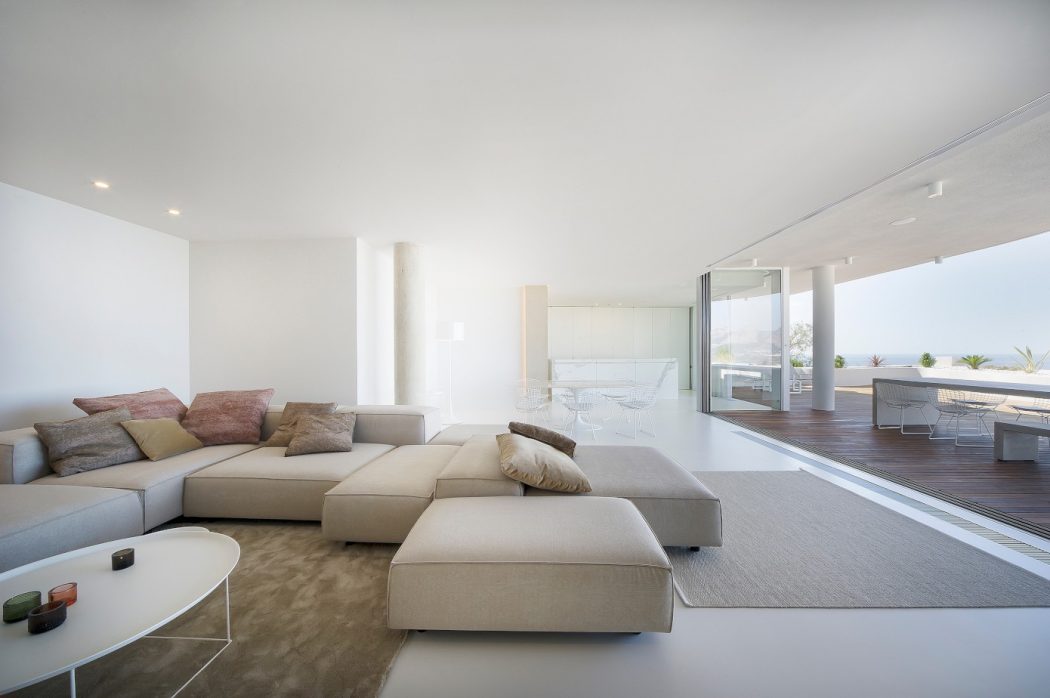 Spacious, minimalist living room with beige sectional sofa, glass doors leading to balcony.