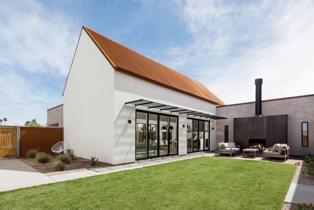 A modern, minimalist home with a distinct roofline, glass walls, and an outdoor lounge area.
