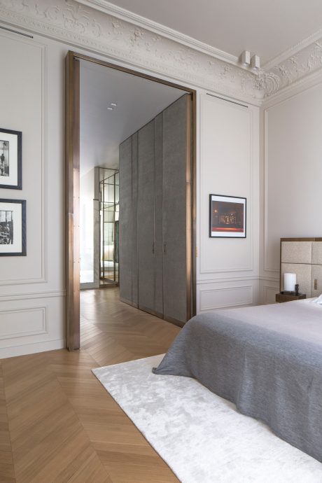 Elegant bedroom with intricate moldings, mirrored closet doors, and herringbone wood floors.