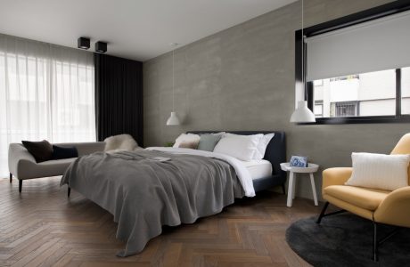 Spacious modern bedroom with gray walls, wooden flooring, and furnishings in neutral colors.