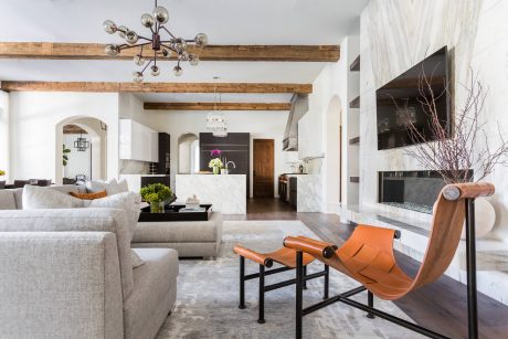The image showcases a modern, open-concept living space with exposed wooden beams, a chandelier, and an orange-hued chair.