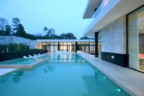 A modern, minimalist home with a large pool and glass walls reflecting the sky.