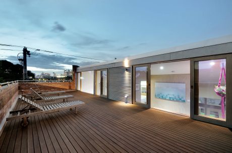 Expansive rooftop deck with wooden floors, glass walls, and city skyline view.