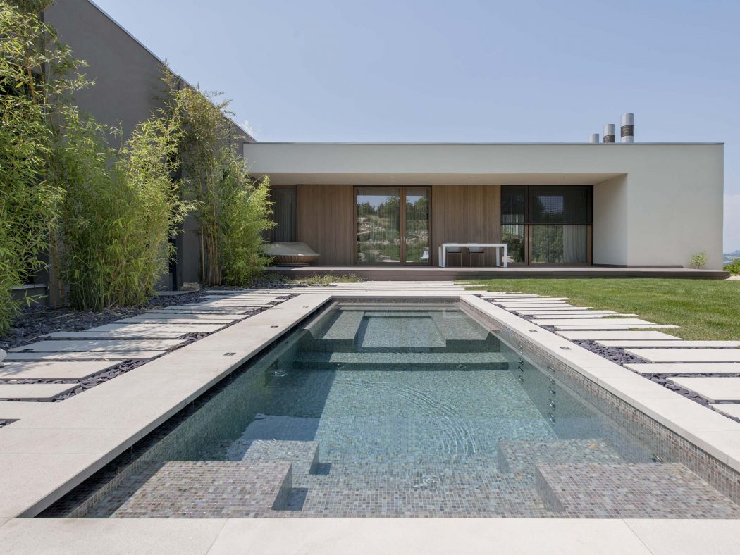 A modern architectural design with a rectangular pool, paved walkway, and lush foliage.