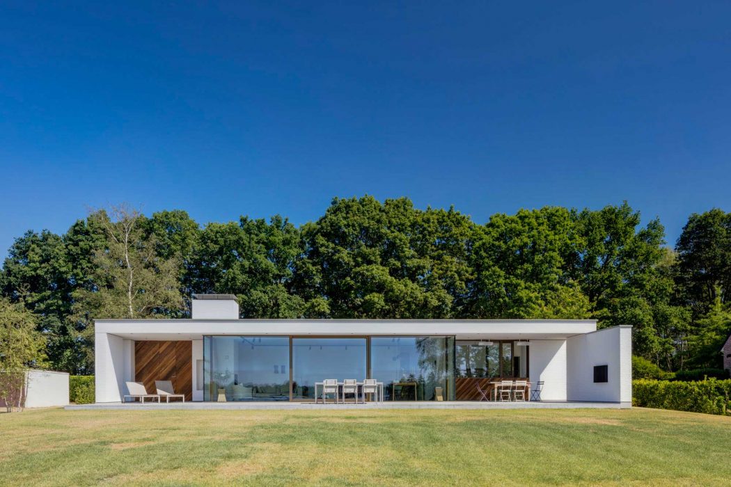 Single-story modern house with glass walls, wood accents, and a spacious lawn.