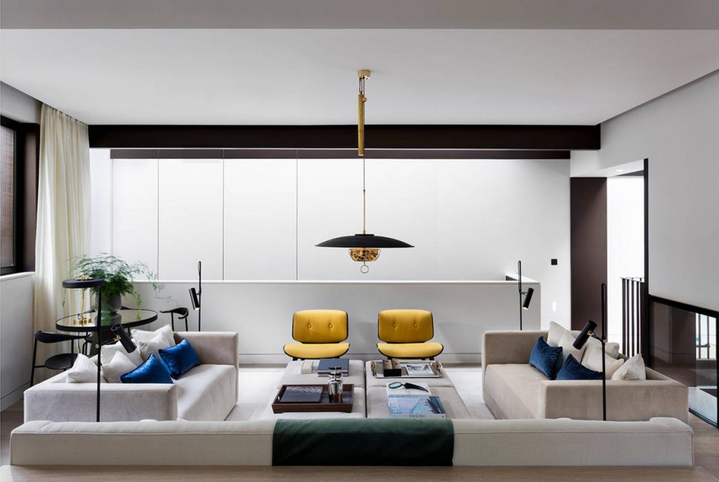 Modern living room with sleek, minimalist design featuring plush sofas, bright yellow chairs, and a statement pendant light.