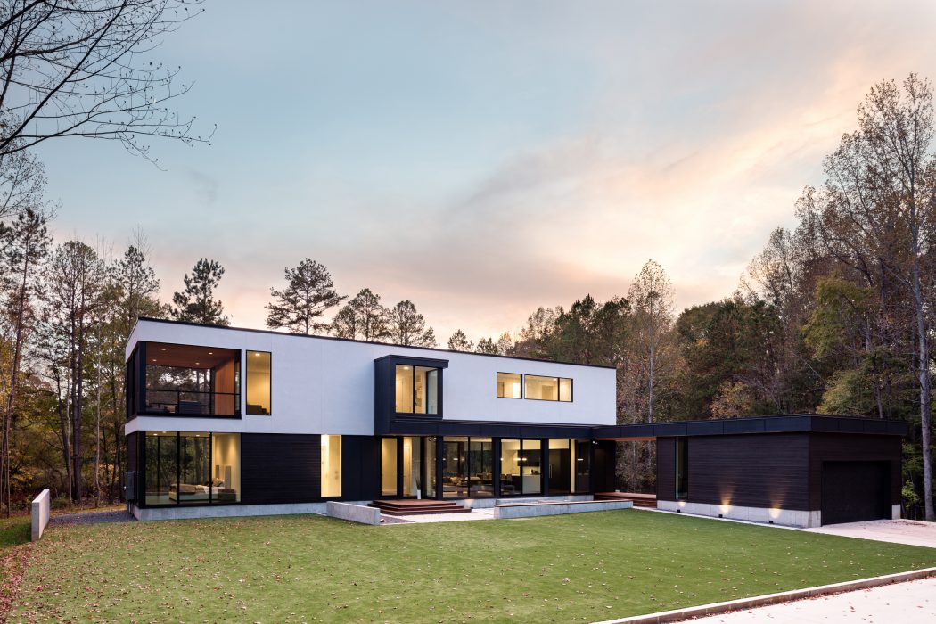 Striking two-story modern home with expansive glass walls, wooden accents, and lush landscaping.