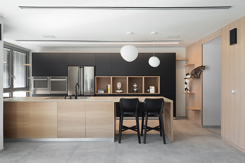 A modern kitchen with stylish black and wood tones, pendant lighting, and built-in shelves.